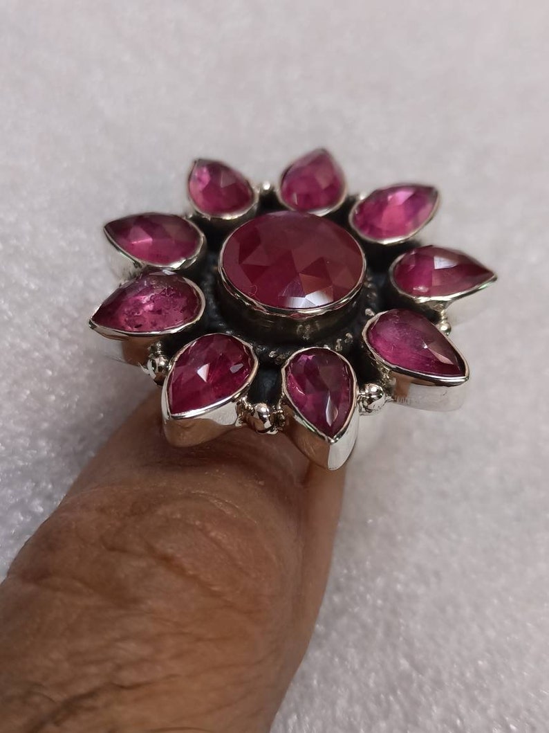 May include: A silver ring with a large pink gemstone surrounded by smaller pink gemstones. The ring is set in a flower design.