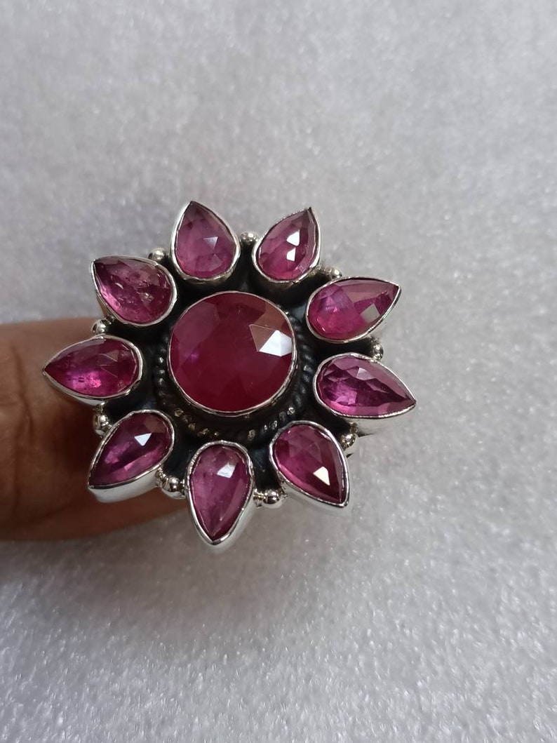 May include: A silver ring with a large pink gemstone surrounded by smaller pink gemstones in a flower shape.
