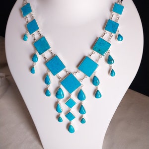 May include: A turquoise and silver necklace with square and teardrop shaped stones. The necklace is displayed on a white mannequin bust.