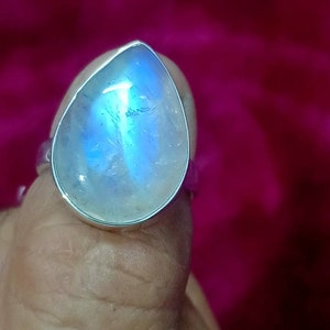 May include: A silver ring with a teardrop-shaped moonstone. The stone has a blue iridescent sheen.