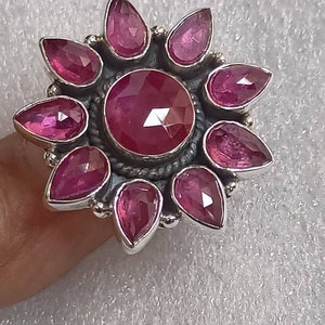 May include: A silver ring with a large pink gemstone surrounded by smaller pink gemstones in a flower shape.