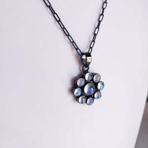 May include: A silver necklace with a black chain and a pendant featuring a cluster of round, iridescent moonstone gems.