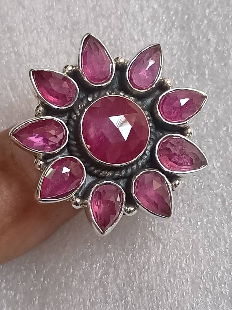May include: A silver ring with a large pink gemstone surrounded by smaller pink gemstones in a flower shape.