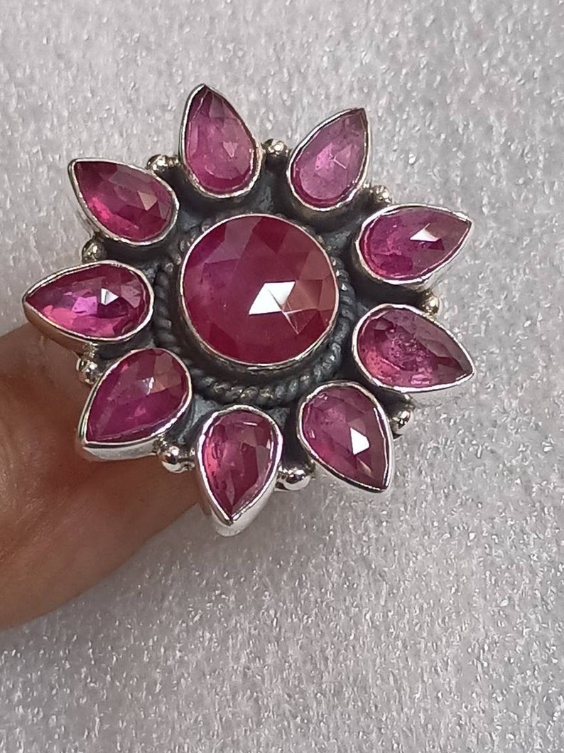 May include: A silver ring with a large pink gemstone surrounded by smaller pink gemstones in a flower shape.