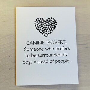 May include: A white card with black text and a black paw print heart design. The text reads "Canine Introvert: Someone who prefers to be surrounded by dogs instead of people."