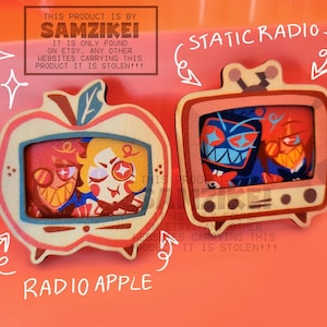 Może przedstawiać: Dwie drewniane przypinki w kształcie telewizorów. Lewa przypinka to telewizor w kształcie jabłka z napisem RADIO APPLE i postacią w środku. Prawa przypinka to prostokątny telewizor z napisem STATIC RADIO i dwiema postaciami.