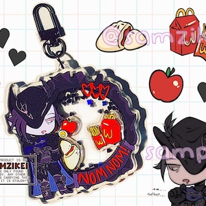 May include: A clear acrylic shaker keychain featuring a cartoon character in a dark hat and outfit, surrounded by floating black heart-shaped sequins. The design includes a red apple, french fries, and a bun, with the text "NOM NOM!" printed on it.