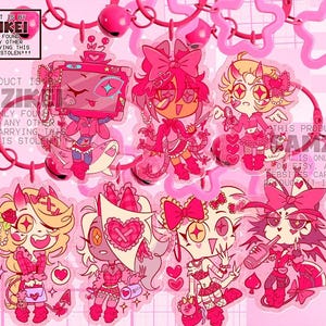 Può includere: Una collezione di sette ciondoli in acrilico a tema rosa raffiguranti vari personaggi dei cartoni animati con cuori, fiocchi e accessori. I ciondoli sono fissati a chiusure a forma di stella e campanellini rosa. Il testo recita THIS PRODUCT IS BY SAMZIKEI.