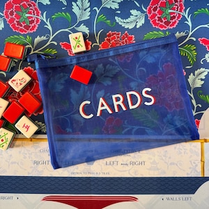 May include: A blue mesh zippered pouch with the word "CARDS" in white and red lettering. The pouch is filled with a game, and surrounded by game tiles and a floral patterned background.