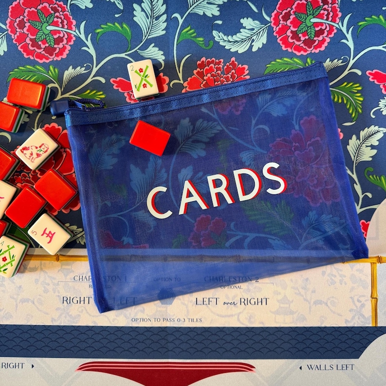 May include: A blue mesh zippered pouch with the word "CARDS" in white and red lettering. The pouch is filled with a game, and surrounded by game tiles and a floral patterned background.
