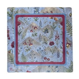 May include: A square scarf featuring a light blue background with a repeating pattern of mountains, ferns, red poppies, and blue wildflowers. The design is framed by a thick maroon border surrounded by a light blue border, with a small logo in the corner.