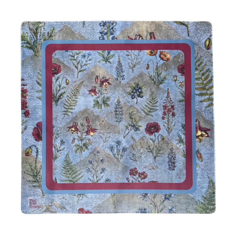 May include: A square scarf featuring a light blue background with a repeating pattern of mountains, ferns, red poppies, and blue wildflowers. The design is framed by a thick maroon border surrounded by a light blue border, with a small logo in the corner.
