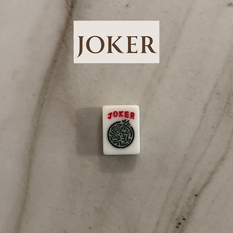 May include: A white Mahjong tile with the word "JOKER" in red and a green circular design. Above the tile is a rectangular sign with the word "JOKER" in brown.