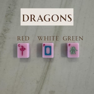 May include: Three pink Mahjong tiles with red, white, and green symbols. The tiles are labeled "RED", "WHITE", and "GREEN". The word "DRAGONS" is written above the tiles in a rectangular box.