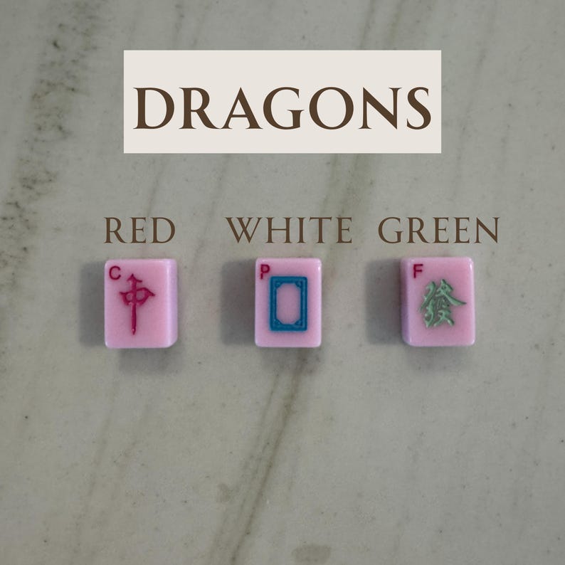 May include: Three pink Mahjong tiles with red, white, and green symbols. The tiles are labeled "RED", "WHITE", and "GREEN". The word "DRAGONS" is written above the tiles in a rectangular box.