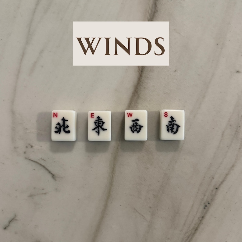 May include: Four white Mahjong tiles with black Chinese characters and red accents, labeled N, E, W, and S, representing the cardinal directions. The word "WINDS" is above the tiles. The tiles are on a marble surface.