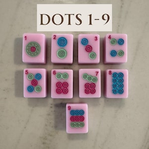 May include: Nine pink mahjong tiles with colorful dot designs, numbered 1 through 9. The tiles feature green, blue, and red circular patterns. The text "DOTS 1-9" is displayed at the top of the image.
