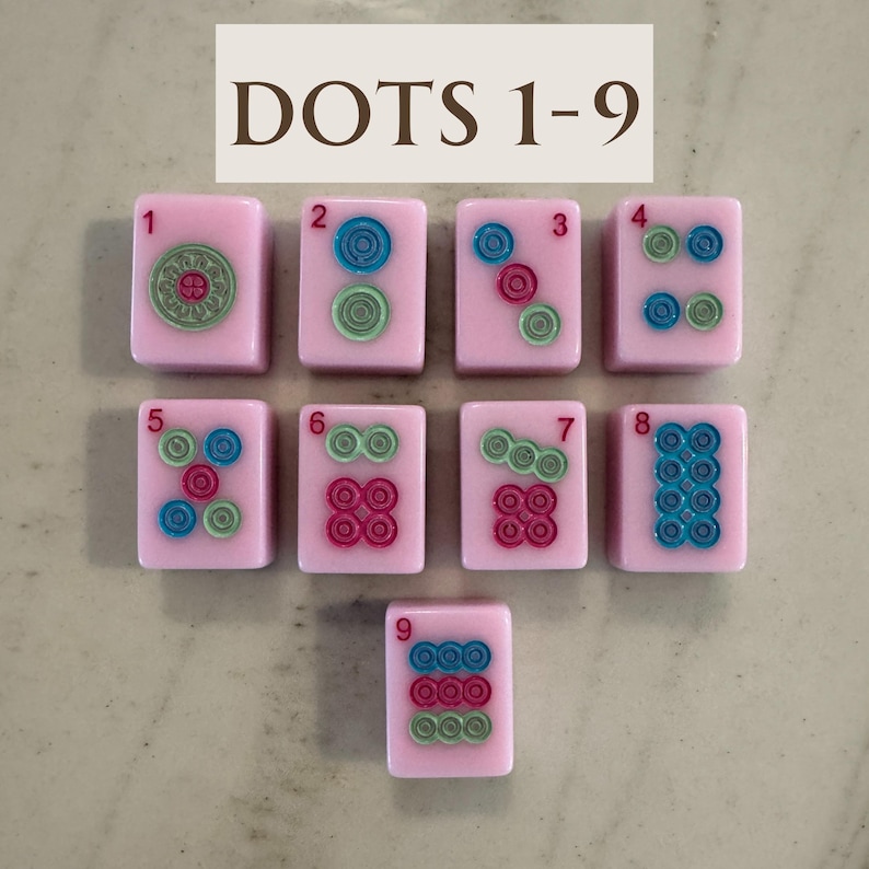 May include: Nine pink mahjong tiles with colorful dot designs, numbered 1 through 9. The tiles feature green, blue, and red circular patterns. The text "DOTS 1-9" is displayed at the top of the image.