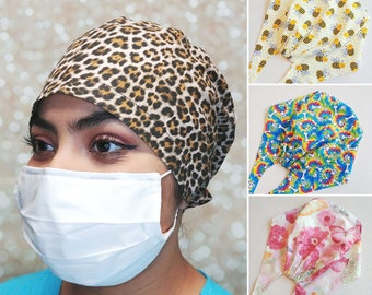 May include: A person wearing a leopard print scrub cap and a white face mask. Additional scrub caps with bee, tie-dye paw print, and floral butterfly patterns are displayed.