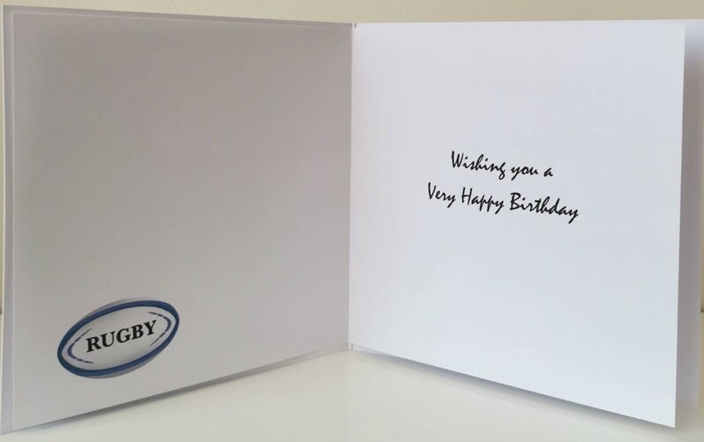 Puede incluir: Tarjeta de cumplea&ntilde;os blanca abierta con el texto "Wishing you a Very Happy Birthday" en escritura negra. Un logotipo de bal&oacute;n de rugby azul y blanco est&aacute; en el lado izquierdo de la tarjeta.