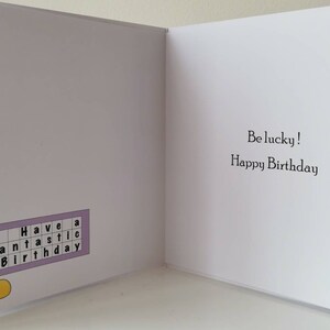 Puede incluir: Tarjeta de felicitaci&oacute;n con tem&aacute;tica de bingo. El lado izquierdo presenta una ilustraci&oacute;n de botella de bingo y una tarjeta de bingo con las palabras "Have a Fantastic Birthday". El lado derecho dice "Be lucky! Happy Birthday".