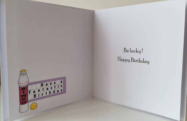 Puede incluir: Tarjeta de felicitaci&oacute;n con tem&aacute;tica de bingo. El lado izquierdo presenta una ilustraci&oacute;n de botella de bingo y una tarjeta de bingo con las palabras "Have a Fantastic Birthday". El lado derecho dice "Be lucky! Happy Birthday".