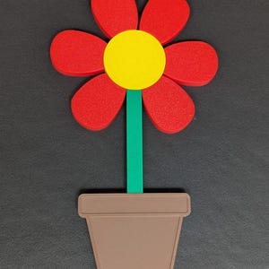 May include: A colorful, stylized flower in a brown pot. The flower has red petals, a yellow center, and a green stem. The pot is a simple, rectangular shape. The image is set against a dark gray background.