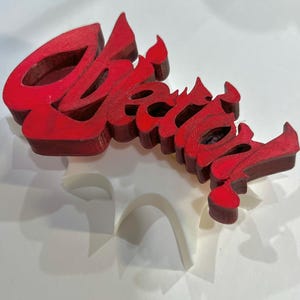 Può includere: Una parola decorativa in legno rosso "Create" in un font stilizzato. La parola è tridimensionale e sembra essere tagliata dal legno. La parola è dipinta in un colore rosso pieno.