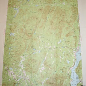 May include: A vintage topographic map of the Schroon Lake area in New York State. The map shows the surrounding mountains, lakes, and rivers. The map is printed on a cream-colored paper with brown and green lines and text. The map is titled "Schroon Lake, N.Y."