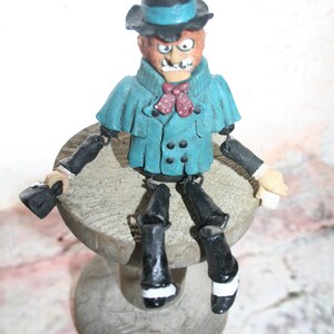 May include: A blue and black figurine of a man wearing a top hat and a bow tie. The figurine is sitting on a wooden base.
