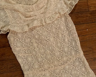 Könnte beinhalten: Ein zartes, cremefarbenes Spitzenkleid mit Rüschen am Ausschnitt und kurzen Ärmeln. Das Kleid ist aus einem feinen, leichten Stoff gefertigt und hat ein zartes Blumenmuster.