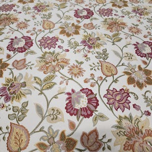 May include: A white fabric featuring a repeating floral pattern with intricate vines and leaves. The design includes blossoms in shades of deep magenta, muted orange, soft yellow, and sage green, all rendered with a textured, woven appearance.
