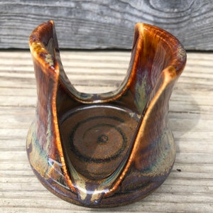 May include: A ceramic dish with a brown, yellow, and blue glaze. The dish has a circular base and two raised sides that form a V-shape. The dish is designed to hold a mug or cup.