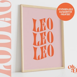 May include: A framed print with a pink background and the name "Leo" written three times in a bold, orange font. The text is in a retro, stylized font. The frame is light wood.