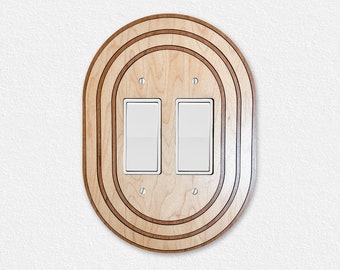 May include: A double light switch plate with a decorative oval wooden frame. The frame has three concentric rings, each with a different wood grain pattern.