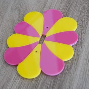 Puede incluir: Una tapa de interruptor de luz en forma de flor rosa y amarilla. La tapa tiene ocho pétalos, que se alternan en color.