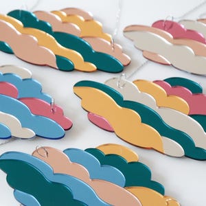 May include: A collection of colorful cloud-shaped necklaces. Each necklace features layered, abstract cloud designs in shades of pink, blue, green, and yellow. The necklaces are suspended by thin silver chains.