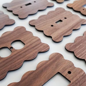 May include: Set of six wooden wall plates in a light brown colour with a wavy edge. The plates have cutouts for electrical outlets and light switches.