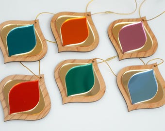 May include: A collection of six decorative ornaments with a leaf-like shape. Each ornament features a wooden frame, a gold-colored inner layer, and a colorful, reflective center in shades of teal, orange, red, green, purple, and blue. Gold string is attached for hanging.