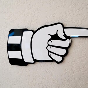 May include: Black and white pointing hand wall decor. The hand is pointing to the right. The hand is stylized and has a simple design.