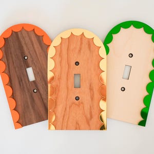 以下が含まれることがあります： フリルエッジの装飾的なライトスイッチカバー3つ。カバーは木でできており、オレンジ、ゴールド、グリーンの異なる色のエッジがあります。