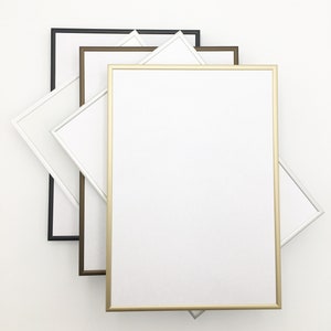 K&ouml;nnte beinhalten: Vier Bilderrahmen in verschiedenen Farben, schwarz, braun, gold und wei&szlig;. Die Rahmen sind &uuml;bereinander gestapelt, wobei der goldene Rahmen vorne liegt.