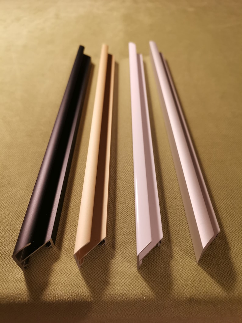 May include: Four different colored picture frame molding samples. The samples are arranged from left to right: black, beige, white, and silver.