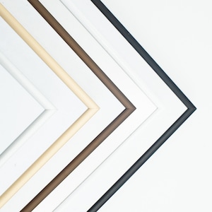 May include: Five picture frames in different colors, from left to right: white, cream, brown, dark brown, and black. The frames are arranged in a diagonal line, with the black frame at the bottom.