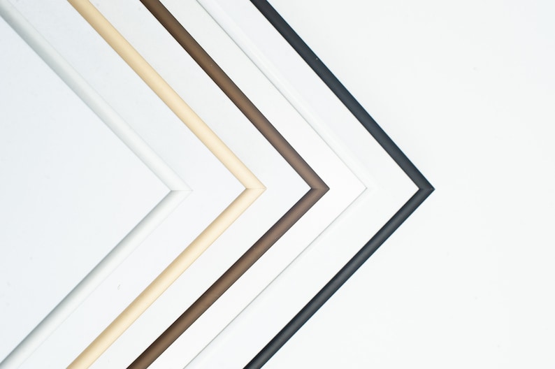 May include: Five picture frames in different colors, from left to right: white, cream, brown, dark brown, and black. The frames are arranged in a diagonal line, with the black frame at the bottom.