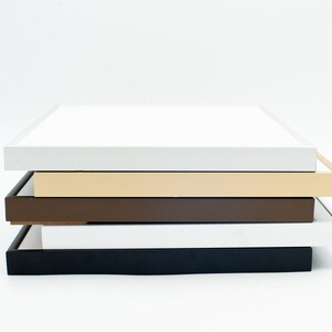May include: Four picture frames stacked on top of each other. The top frame is white, the second frame is beige, the third frame is brown, and the bottom frame is black.