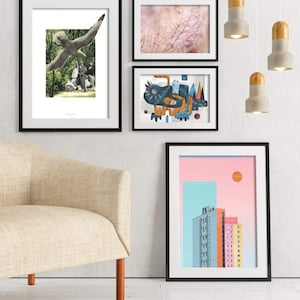May include: Four framed art prints hanging on a white wall above a beige armchair. The prints feature a bird in flight, a close-up of a textured surface, an abstract design with blue, orange, and yellow shapes, and a city skyline with a pink and blue sky.