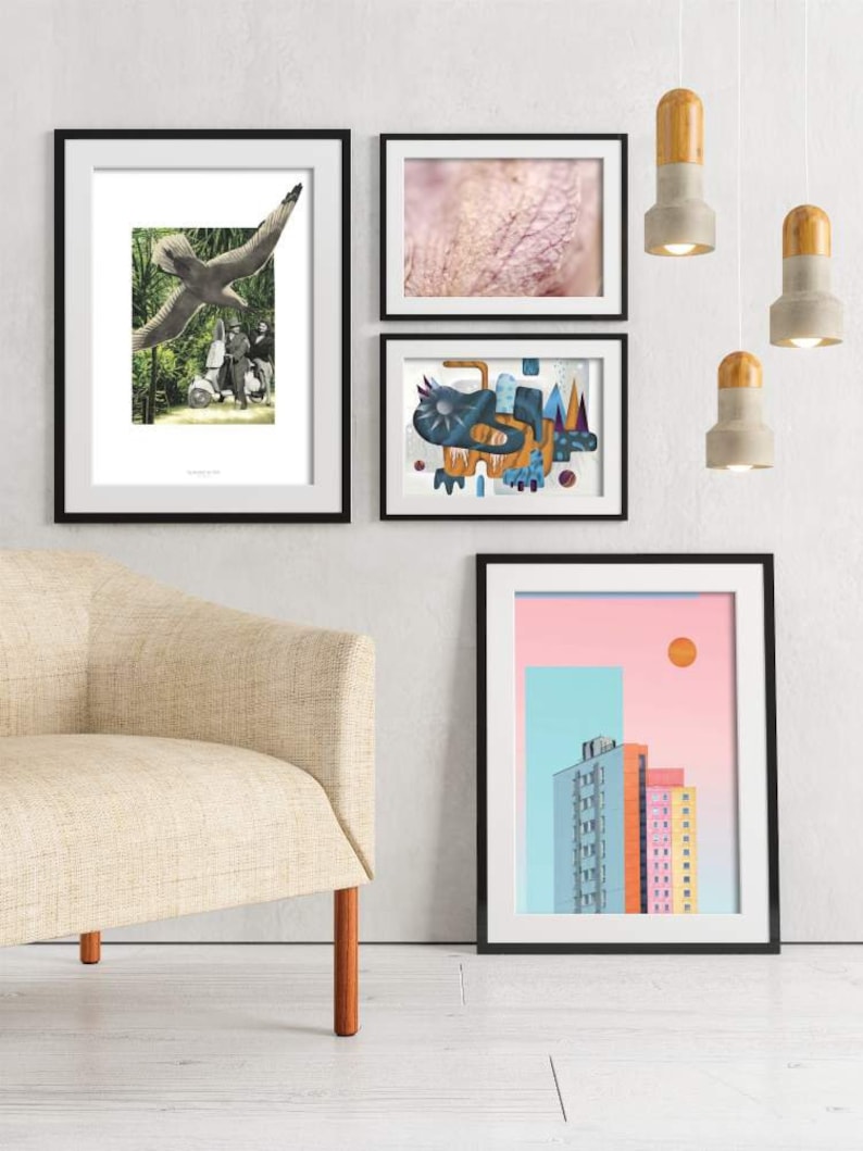 May include: Four framed art prints hanging on a white wall above a beige armchair. The prints feature a bird in flight, a close-up of a textured surface, an abstract design with blue, orange, and yellow shapes, and a city skyline with a pink and blue sky.