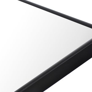 May include: Close-up of the corner of a black framed mirror. The mirror is rectangular and has a smooth, reflective surface.