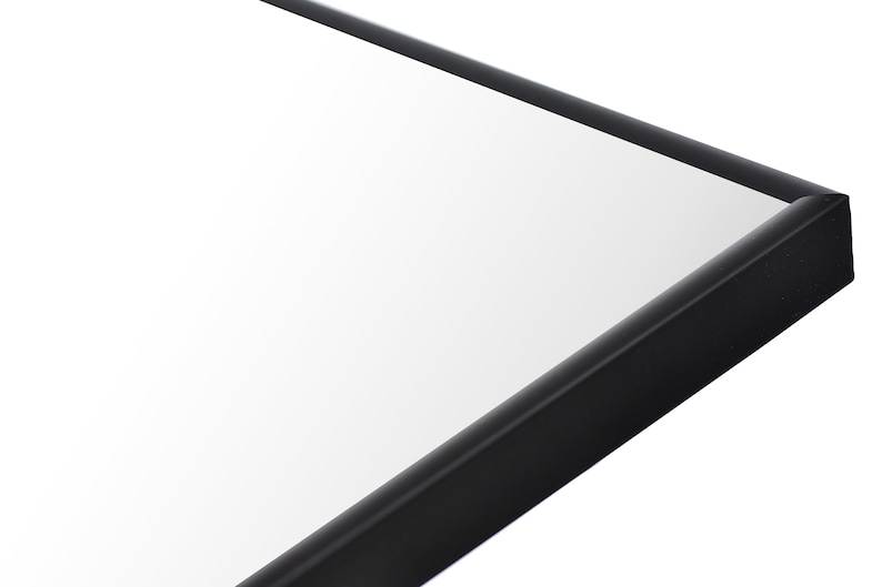 May include: Close-up of the corner of a black framed mirror. The mirror is rectangular and has a smooth, reflective surface.